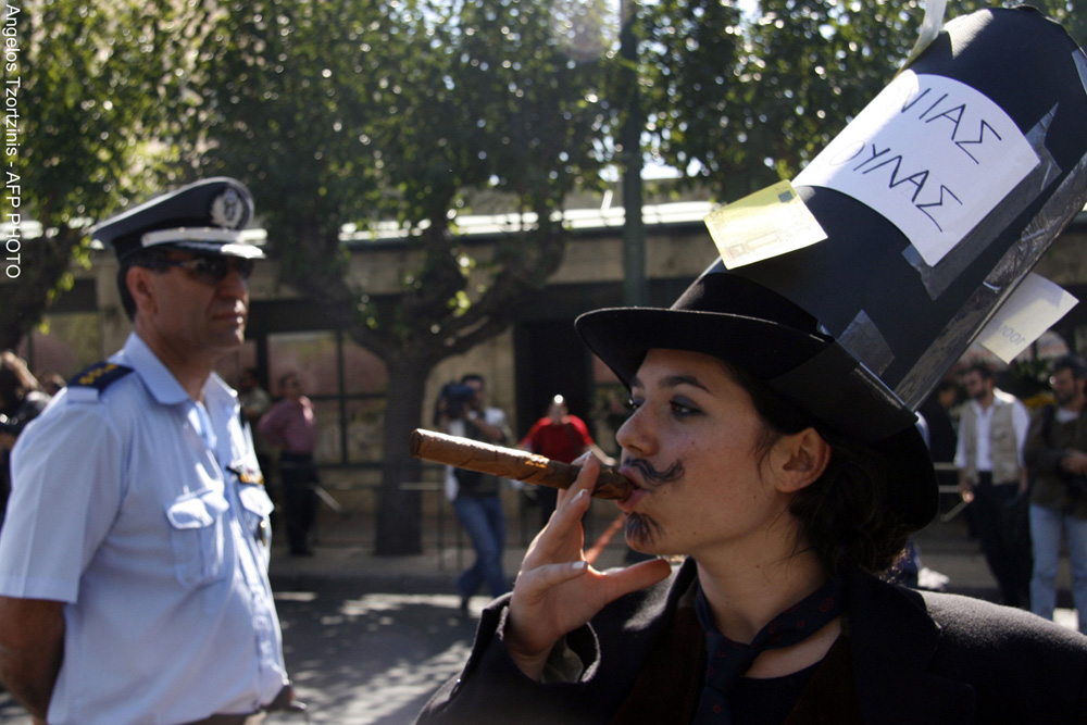 O studentă costumată în om de afaceri fumează trabuc în faţa unui ofiţer de poliţie, în timpul unei manifestaţii studenţeşti desfăşurate la Atena, pe 18 octombrie 2007.