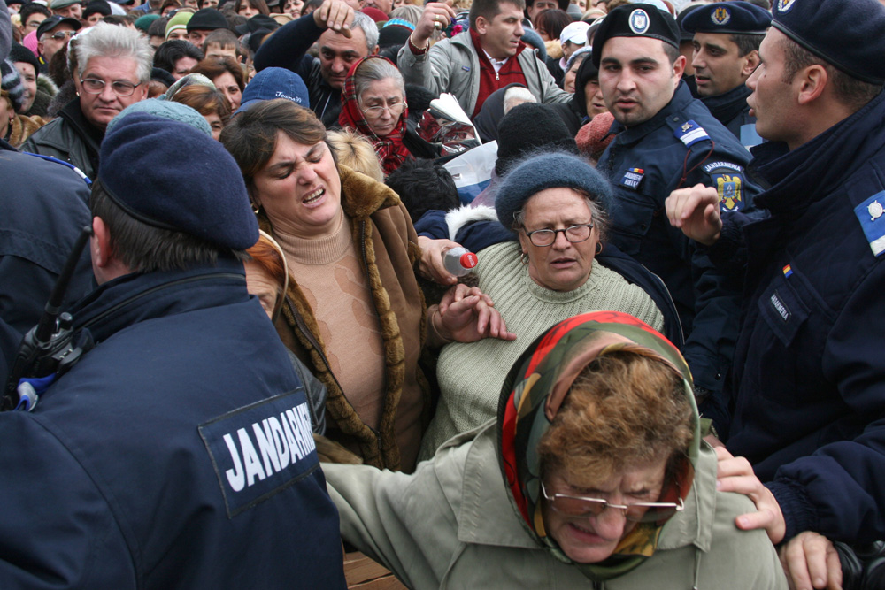 Trei femei încearcă să iasă din mijlocul mulţimii care se înghesuie să participe la slujba de sfinţire a bisericii Mănăstirii Peştera Sfântului Apostol Andrei