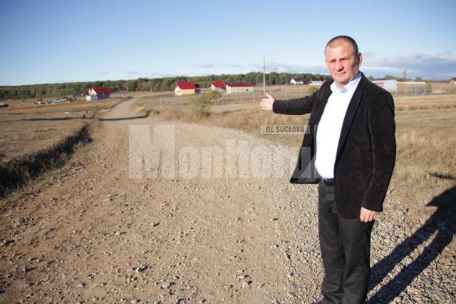 Primarul Viorel Cucu arătând spre drumul care ar fi trebuit să fie betonat de cinci luni