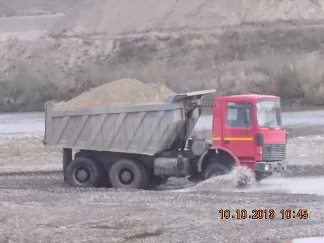 Camioanele firmei, transportând balastul prin apa râului, spre celalalt mal