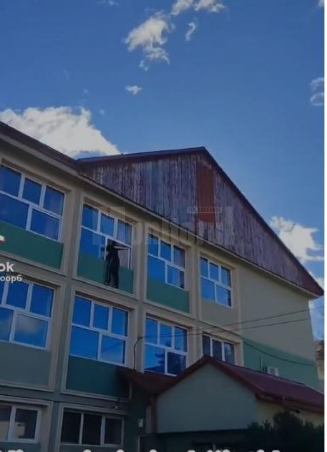 Elev cocoțat pe geam, la exteriorul clădirii